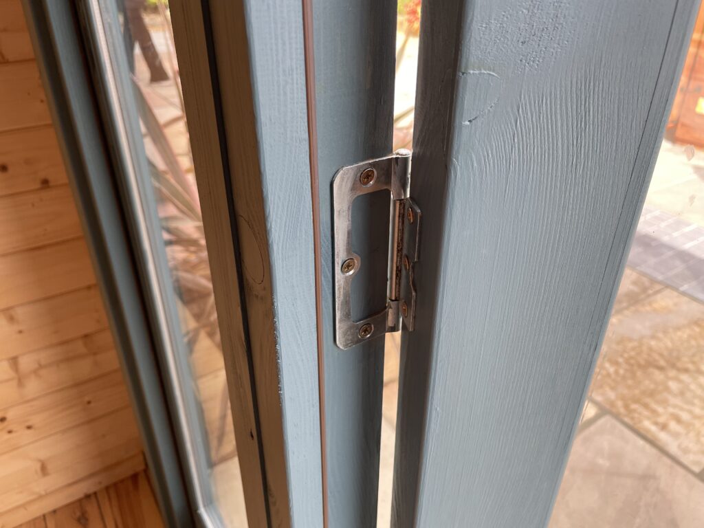 Close-up of metal door hinge and frame detail on Tiger Aura 44 mm Log Cabin at Tong show site.