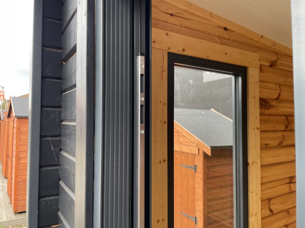Aluminium-framed door and lock detail on the Tiger Black Obsidian 70 mm Insulated Log Cabin at the Horsforth show site showing precision hardware and modern timber finish.
