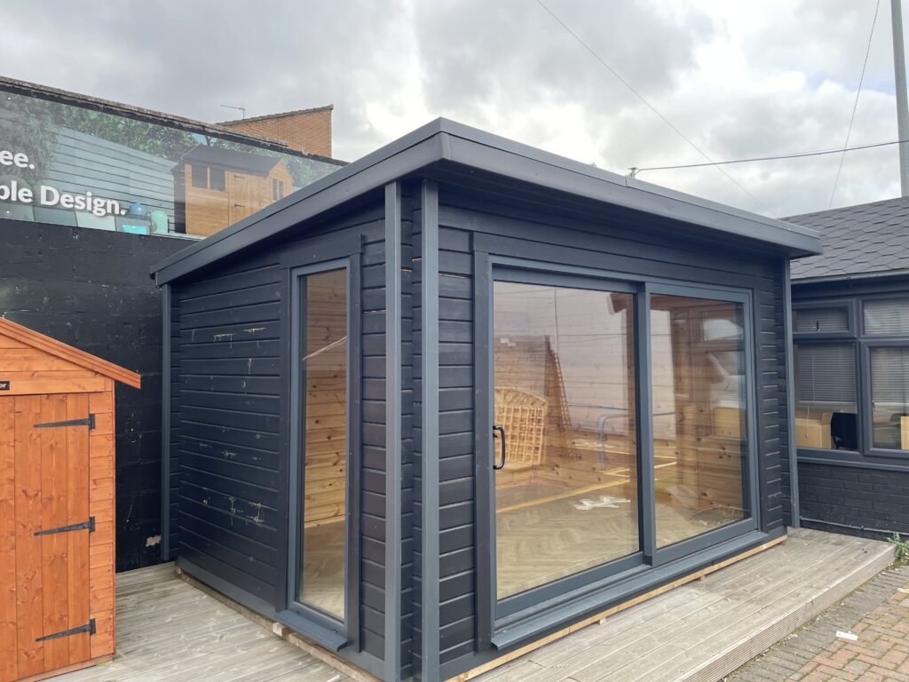 Front and side exterior of the Tiger Black Obsidian 70 mm Insulated Log Cabin at the Horsforth show site showing sliding doors and modern black timber cladding.