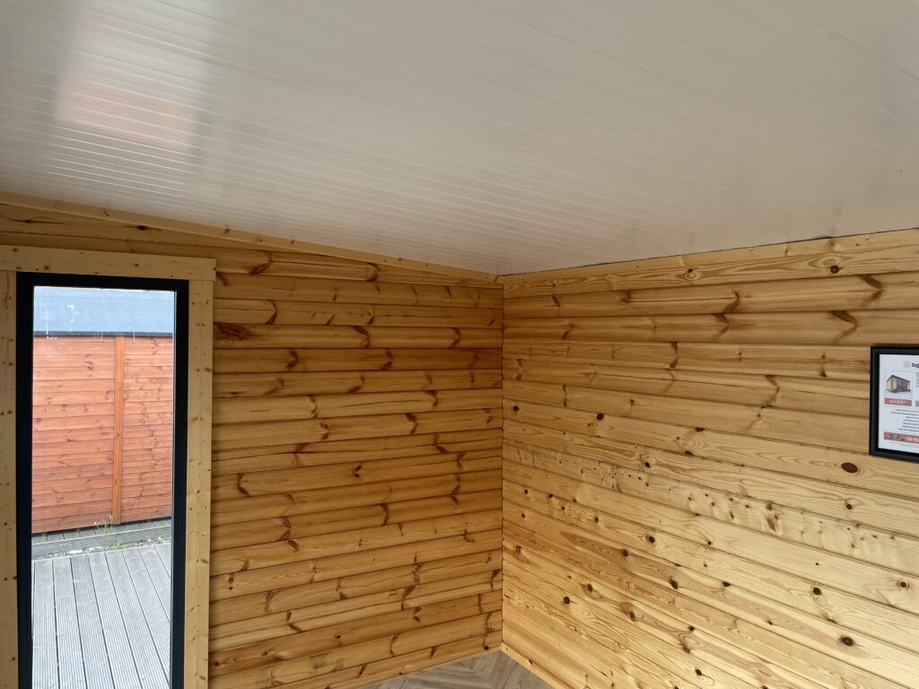 Interior of the Tiger Black Obsidian 70 mm Insulated Log Cabin at the Horsforth show site showing timber walls, white insulated ceiling, and modern window frame.