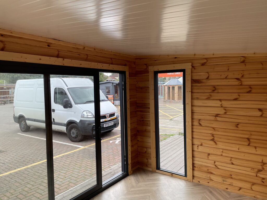 Interior of the Tiger Black Obsidian 70 mm Insulated Log Cabin at the Horsforth show site showing large sliding glass doors, tall side window, and timber cladding.
