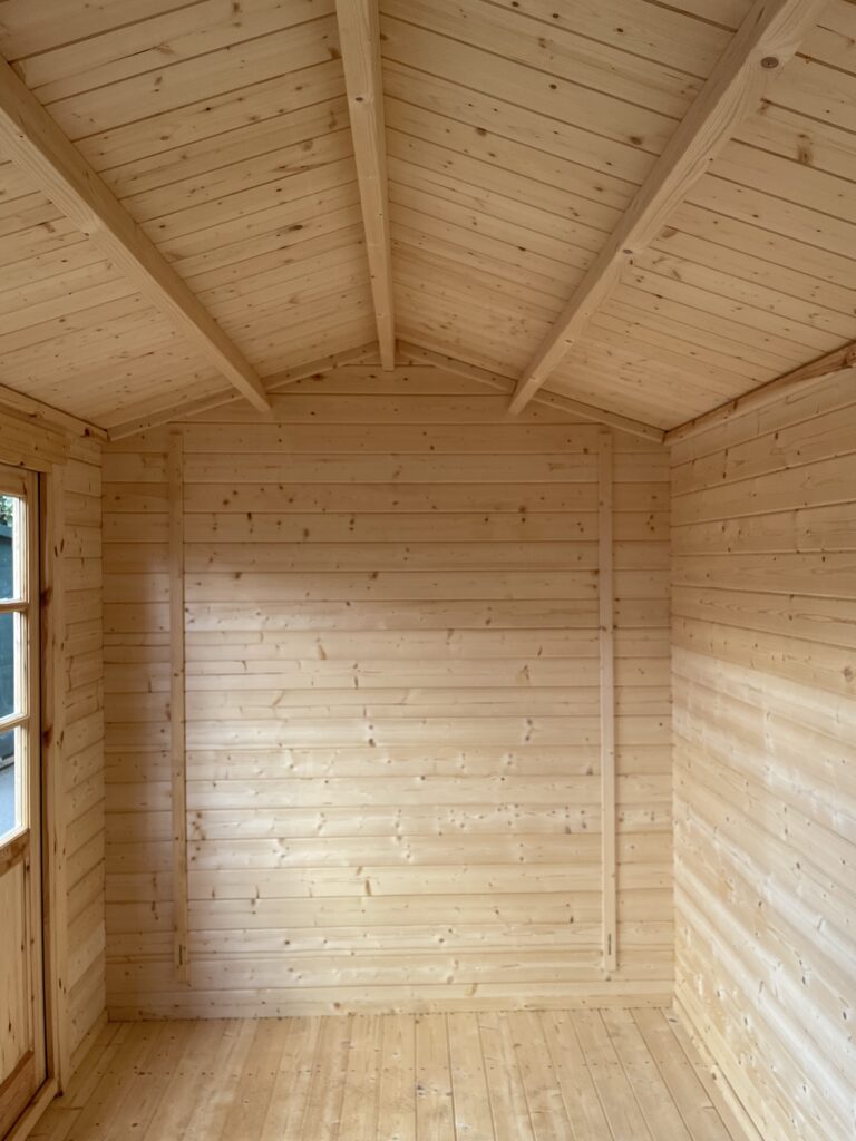 Interior view of the Tiger Persian 28 mm Log Cabin at the Otley show site showing the timber roof beams, tongue-and-groove ceiling, and smooth interior wall panels.