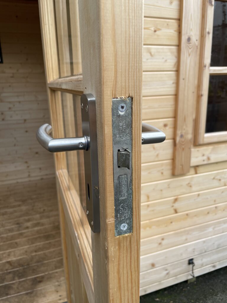 Door lock and handle detail on the Tiger Persian 28 mm Log Cabin at the Otley show site showing stainless steel hardware and timber joinery.