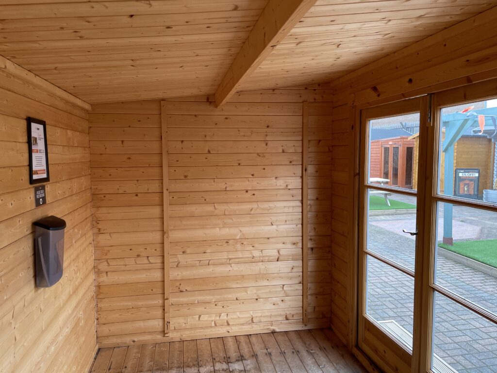 Interior of Tiger Rho 44 mm Log Cabin at Horsforth show site showing timber wall panelling, ceiling beam, and glazed double doors.