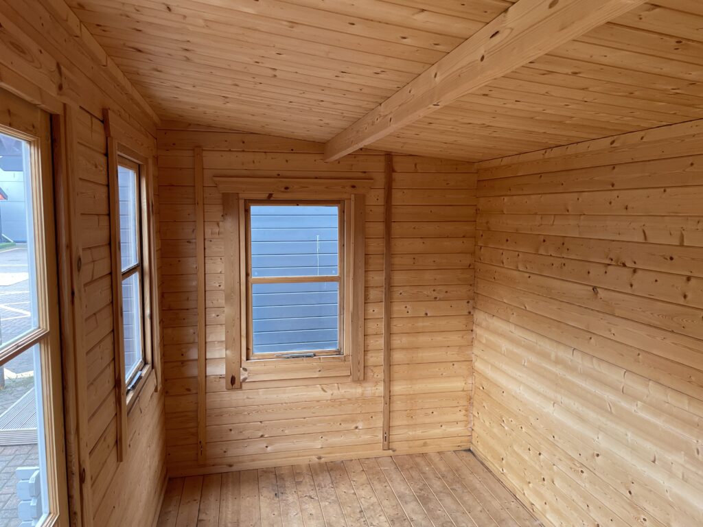 Interior of Tiger Rho 44 mm Log Cabin at Horsforth show site showing timber walls, roof beam, and multiple glazed windows.