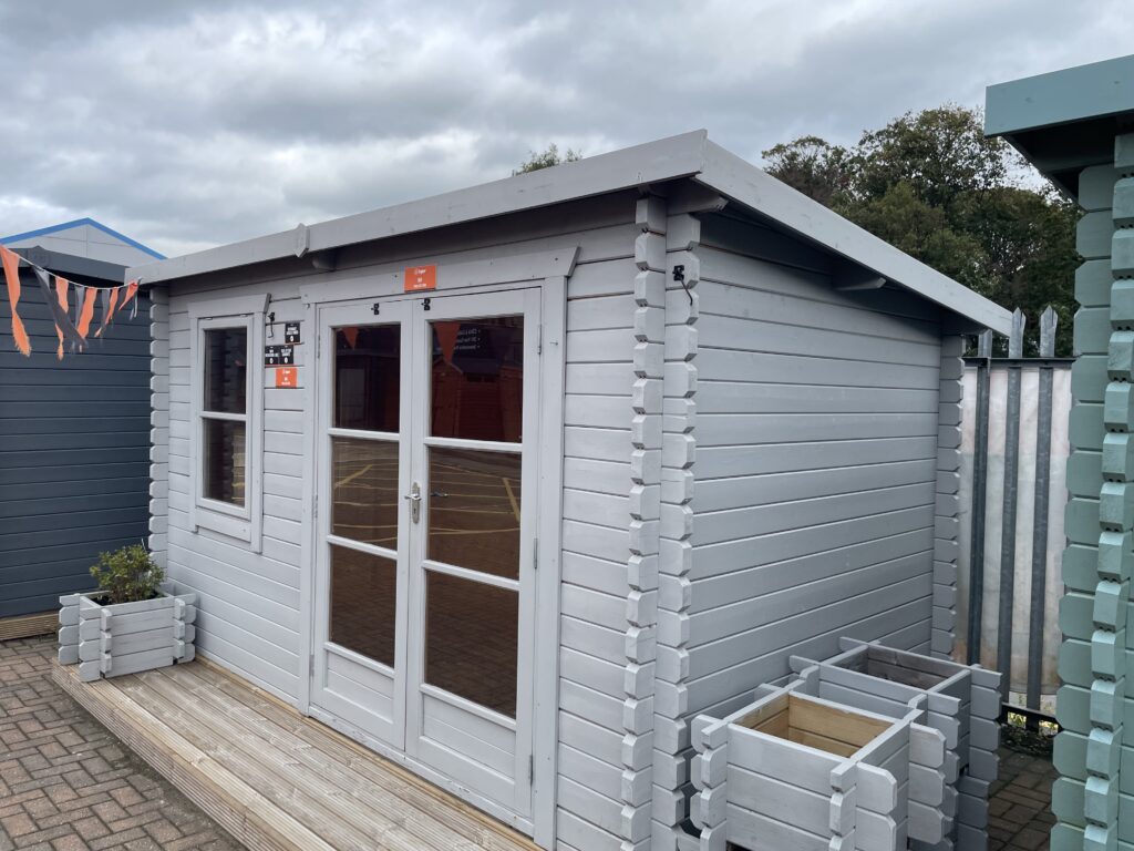 Angled exterior view of Tiger Rho 44 mm Log Cabin showing interlocking log walls, roof overhang, and double doors at Horsforth show site.