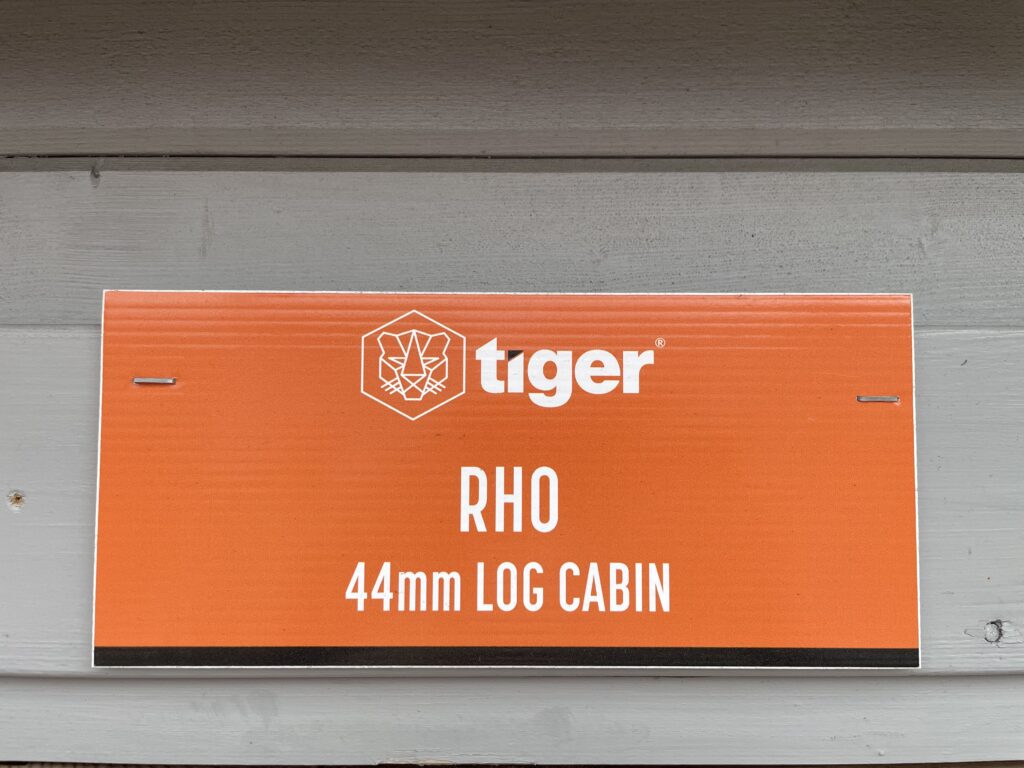 Close-up of Tiger Rho 44 mm Log Cabin orange product sign showing model name and 44 mm log specification at Horsforth show site.