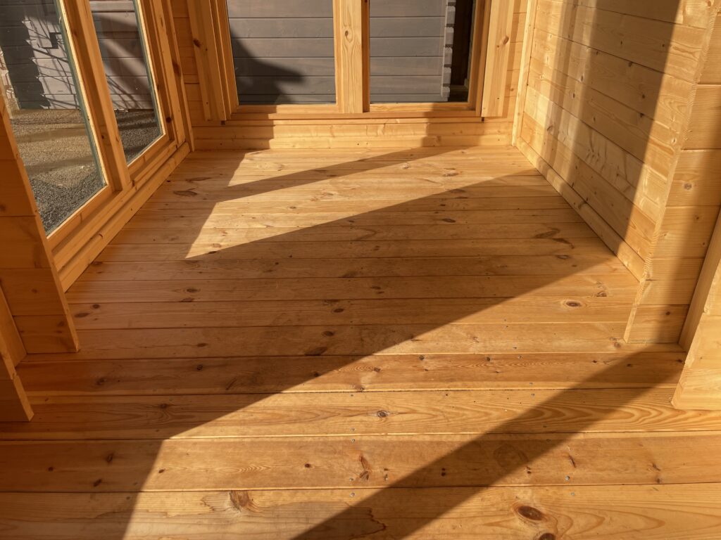 Interior view of the TigerFlex Moda 19 mm Log Cabin at the Otley show site, showing the smooth tongue-and-groove floorboards and natural light from the glazed doors.