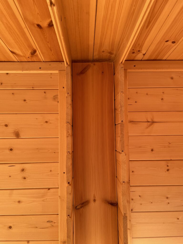 Close-up of the TigerFlex Moda 19 mm Log Cabin interior timber joints at the Otley show site showing the flexible vertical post connection and tongue-and-groove ceiling panels.