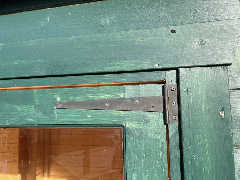 Close-up of a black timber door hinge on a garden building