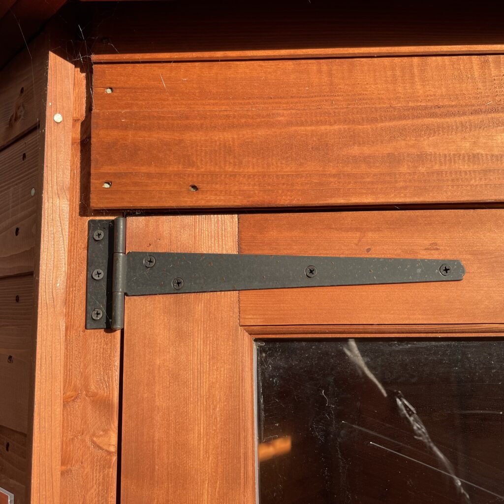 Close-up of a corner joint featuring a black metal hinge on a wooden structure
