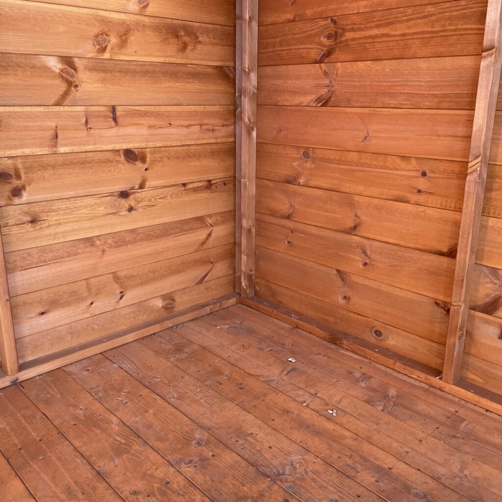 Interior corner of a wooden summerhouse with panelled walls and flooring