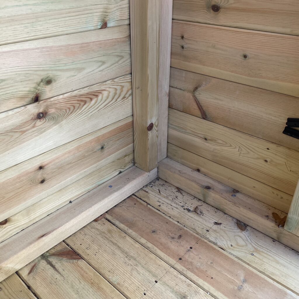 Interior corner of a shed with wooden cladding and floor