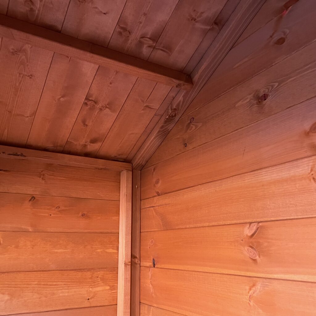 Interior view showing the corner of a wooden garden building with smooth timber panels