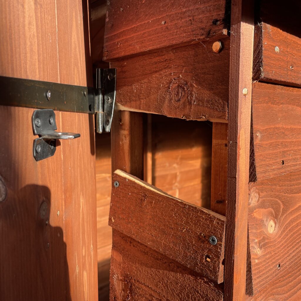 Close-up of a shed door hinge and lock mechanism showing robust construction