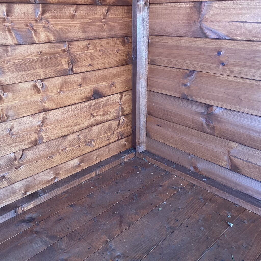 Interior corner of a Tiger Shiplap Apex Shed showing wooden walls and floor