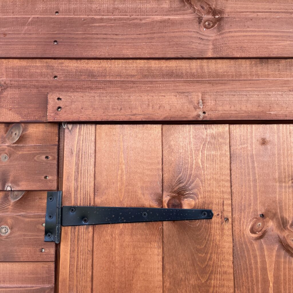 Close-up of a sturdy wooden door with a black metal hinge and latch