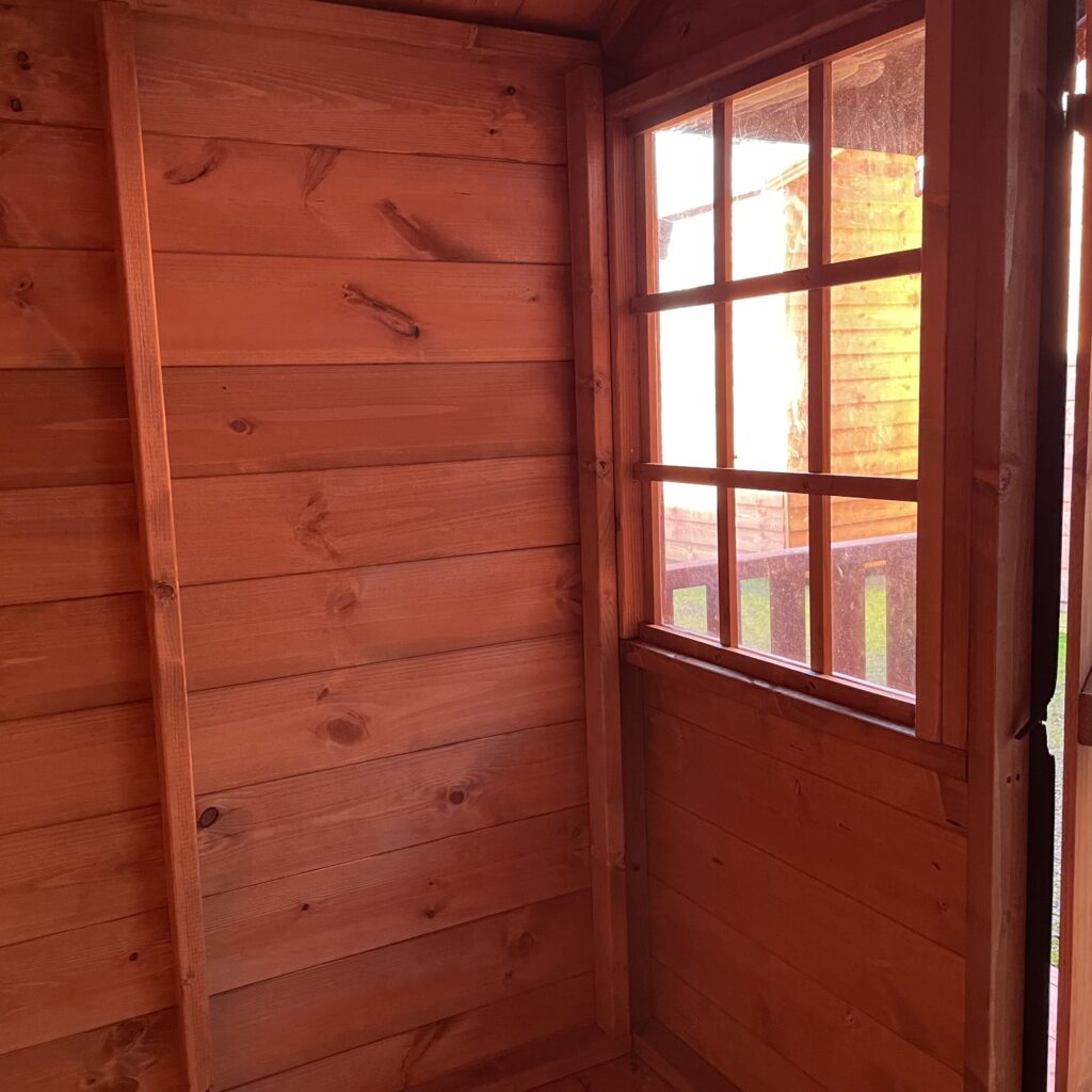 Interior view of the TigerClub Funhouse Playhouse showcasing wooden walls and a grid-style window
