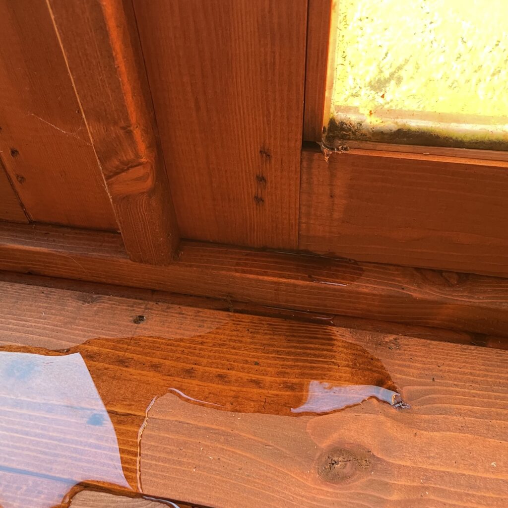 Interior view of a summerhouse with water pooling on the floor near the window frame